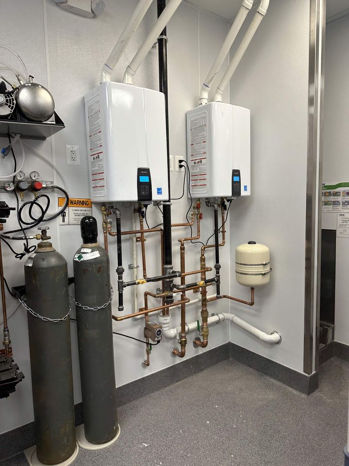 Two wall-mounted tankless water heaters piped in copper with isolation valves and an expansion tank
